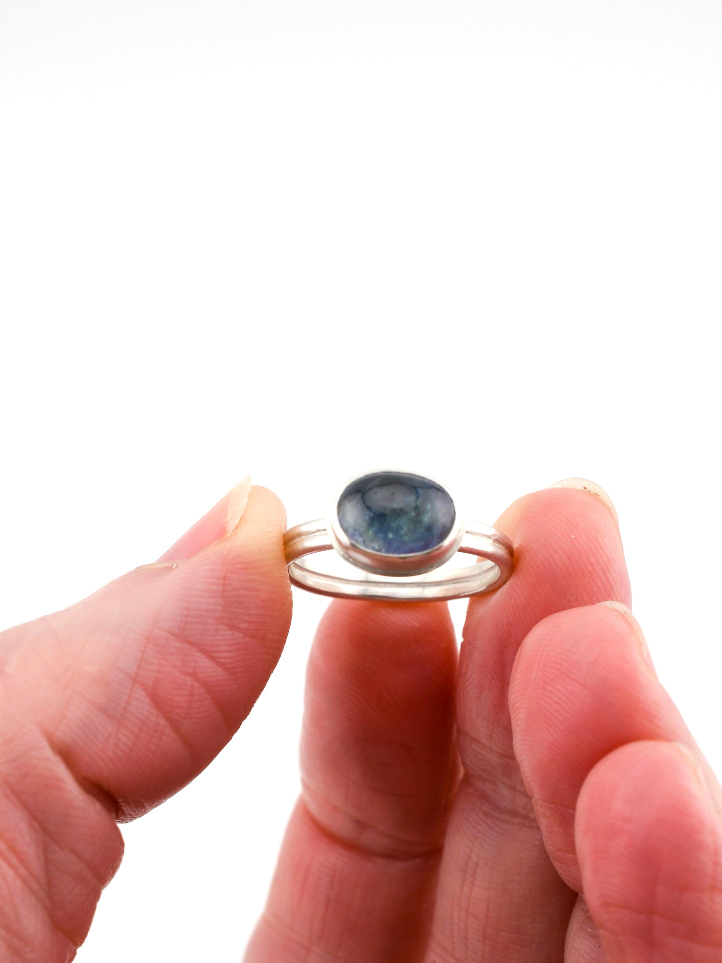 Close-up of a hand holding a silver ring with a blue stone against a white background