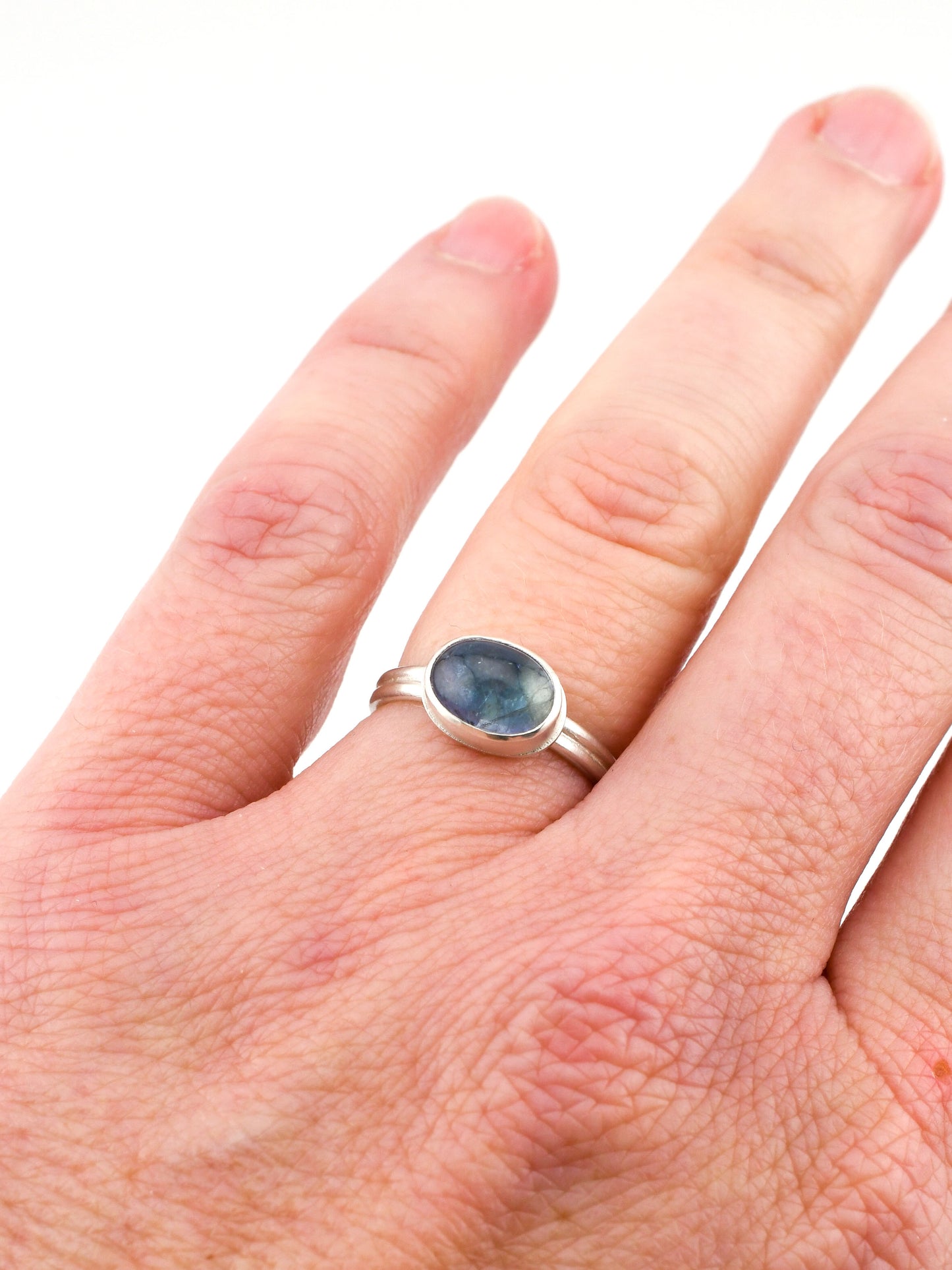 Silver ring with a blue gemstone on a person's finger against a white background