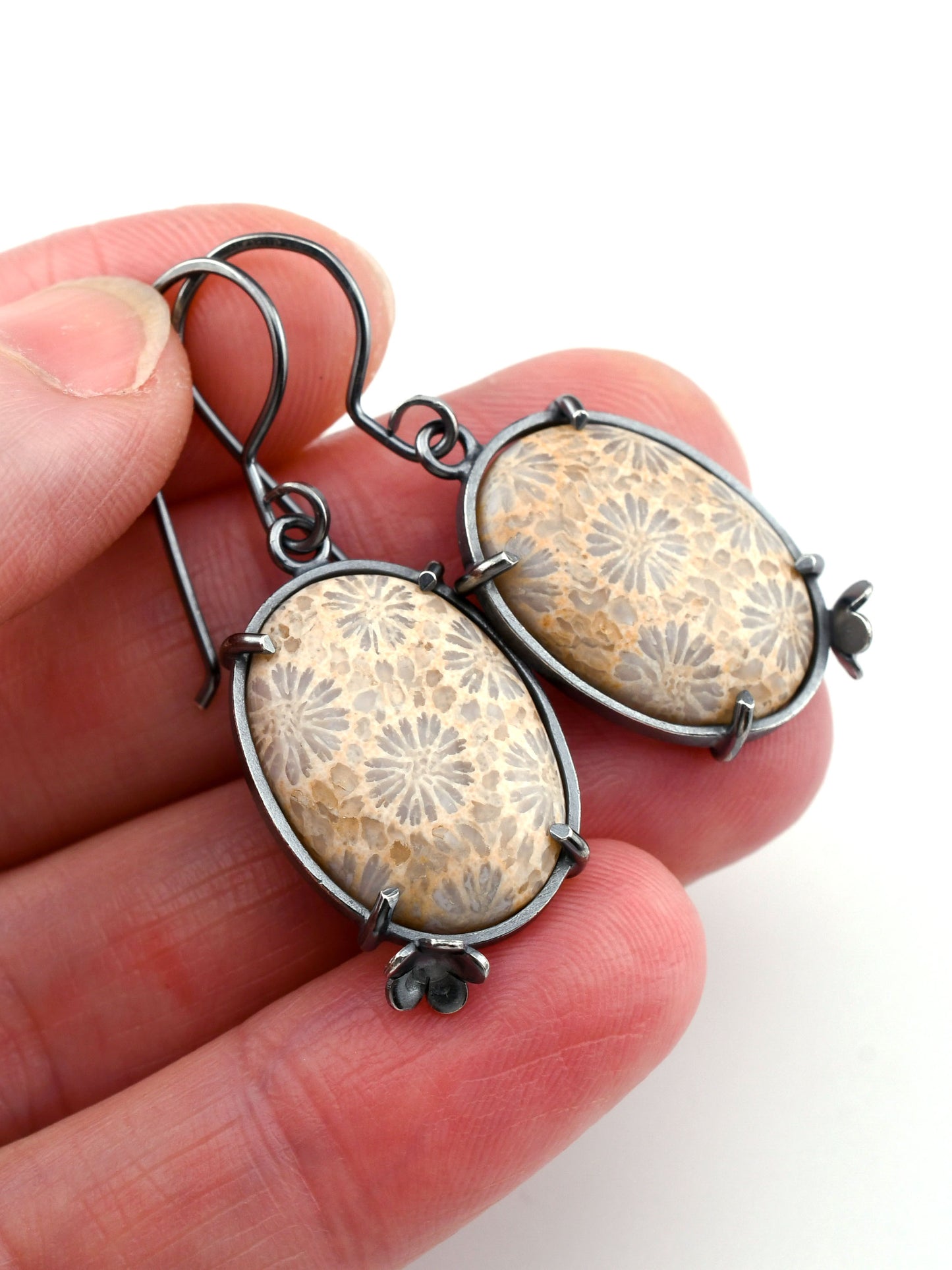 Earrings with floral patterns held between fingers on a white background