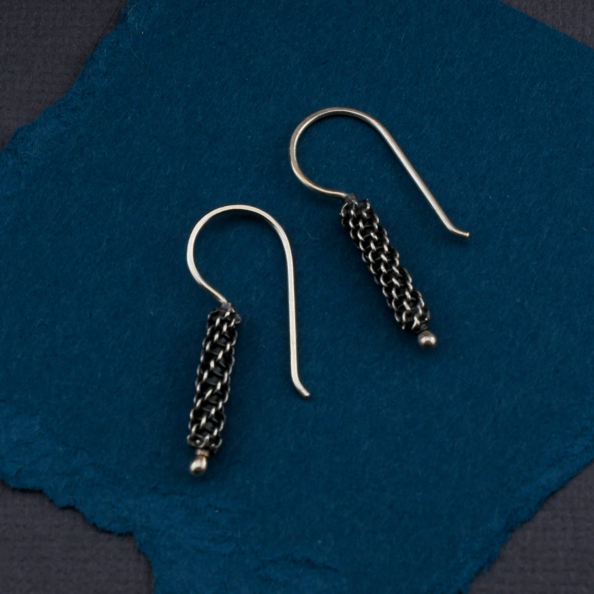 Pair of silver woven earrings on a blue fabric background
