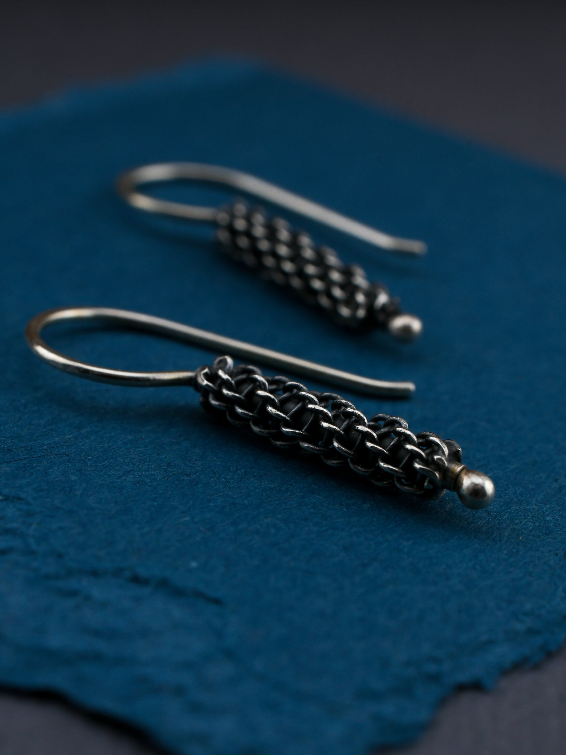 Silver earrings with woven design on a blue textured surface
