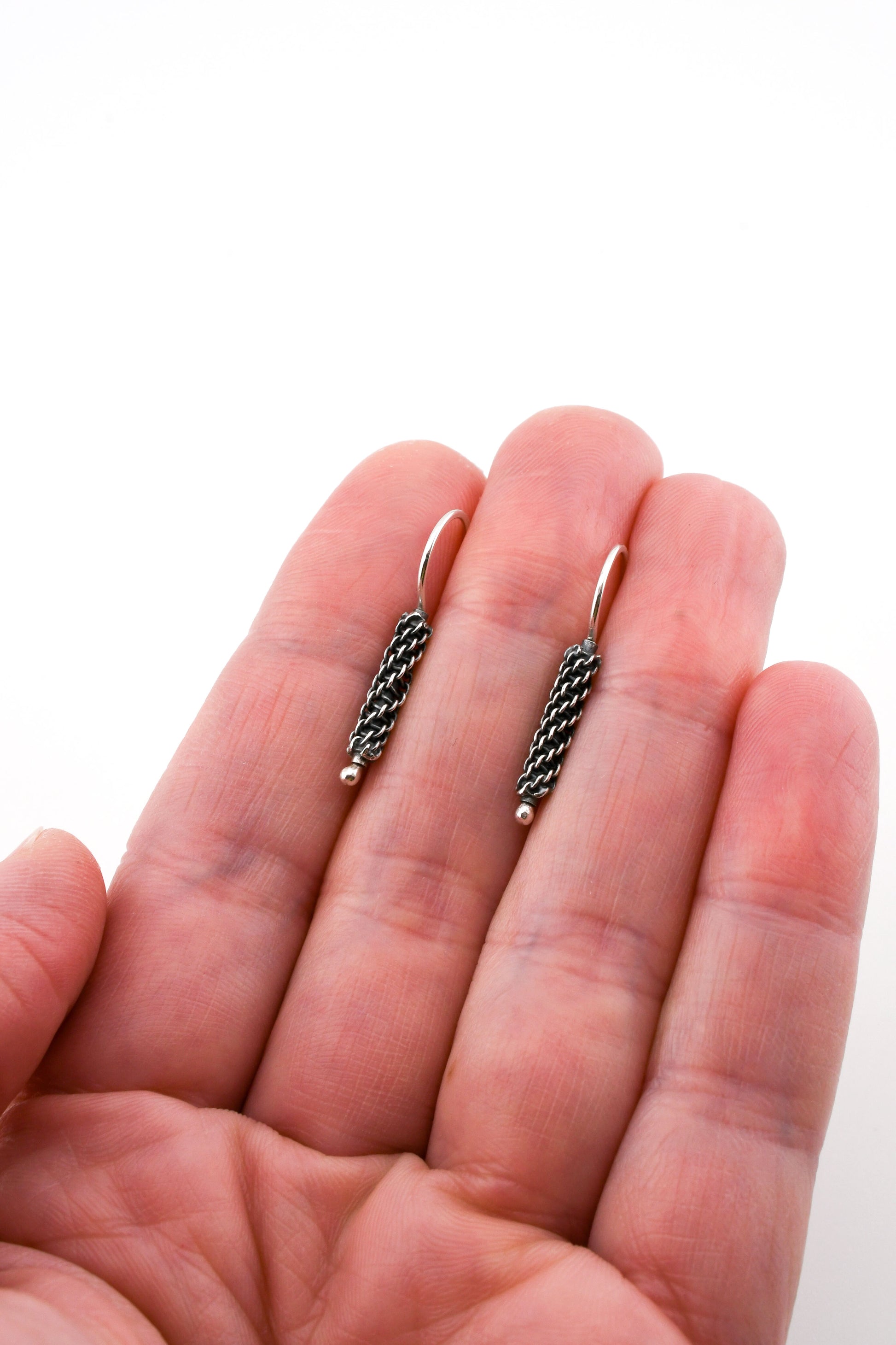 Two small earrings held between fingers on a white background