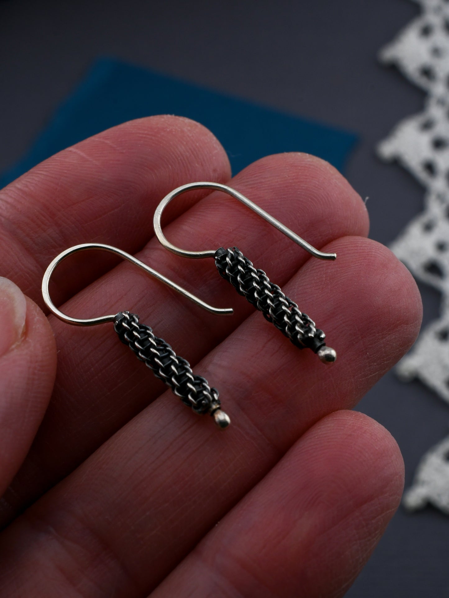 Close-up of a hand holding two silver earrings with woven wire details.