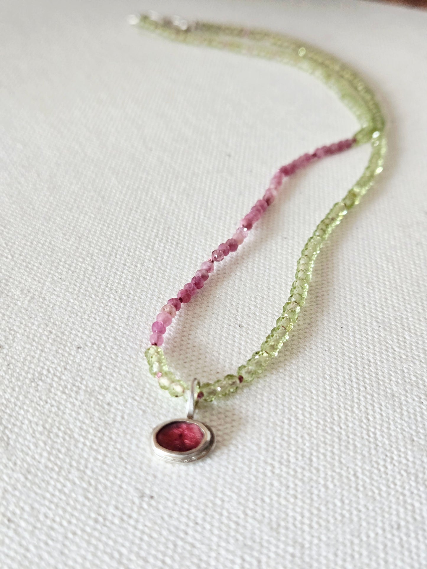 Necklace with pink and green beads on a white fabric background