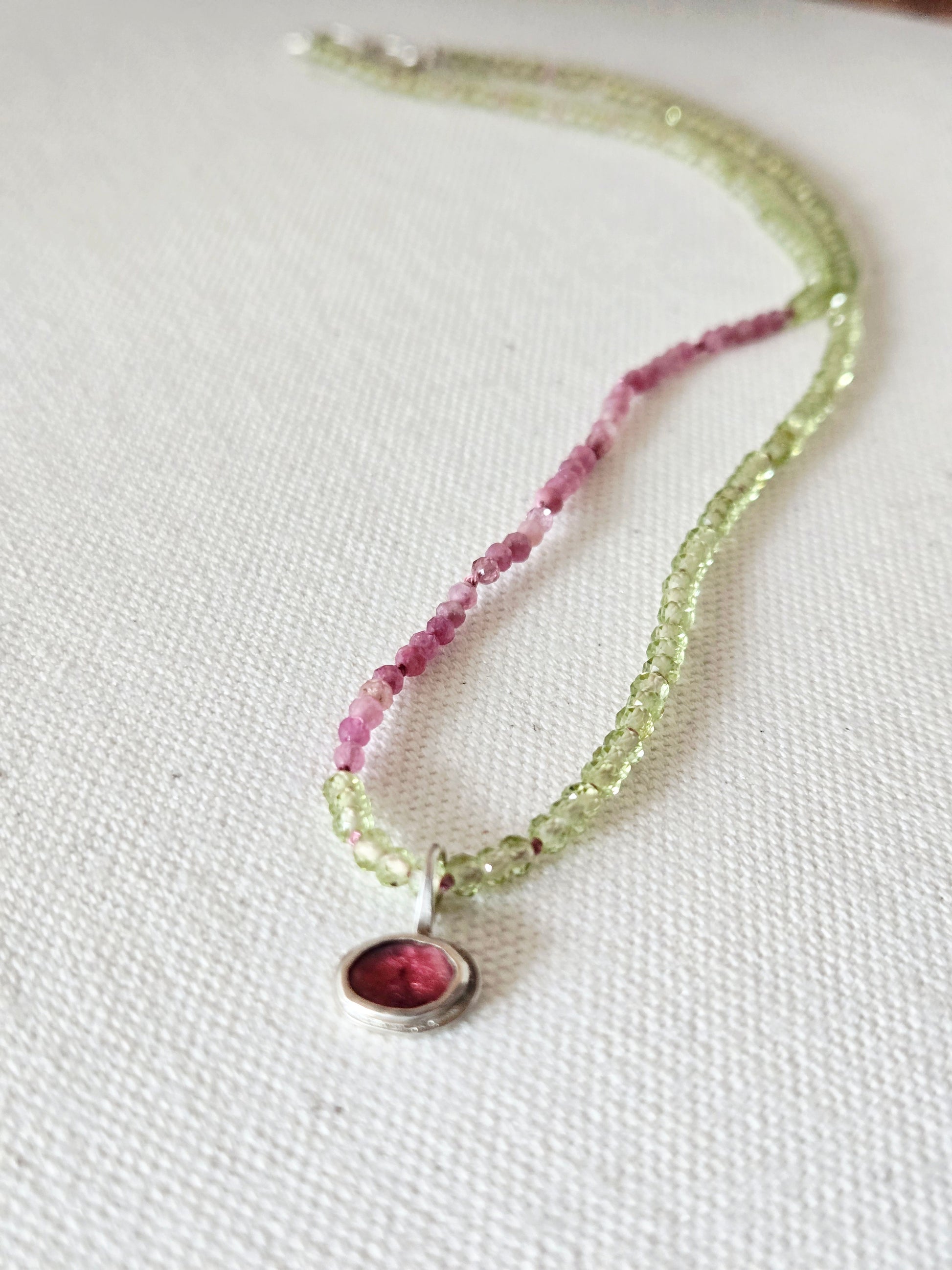 Necklace with pink and green beads on a white fabric background
