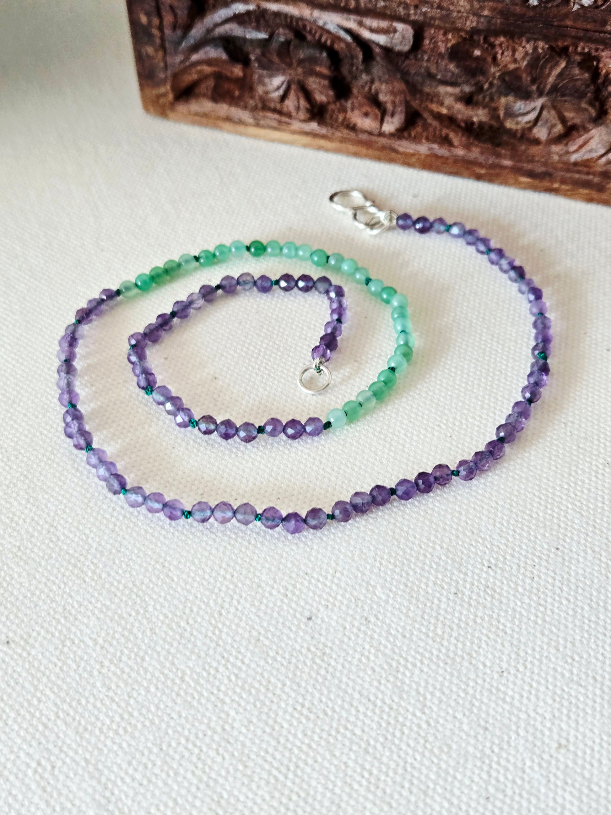 Necklace with purple and green beads on a white fabric background