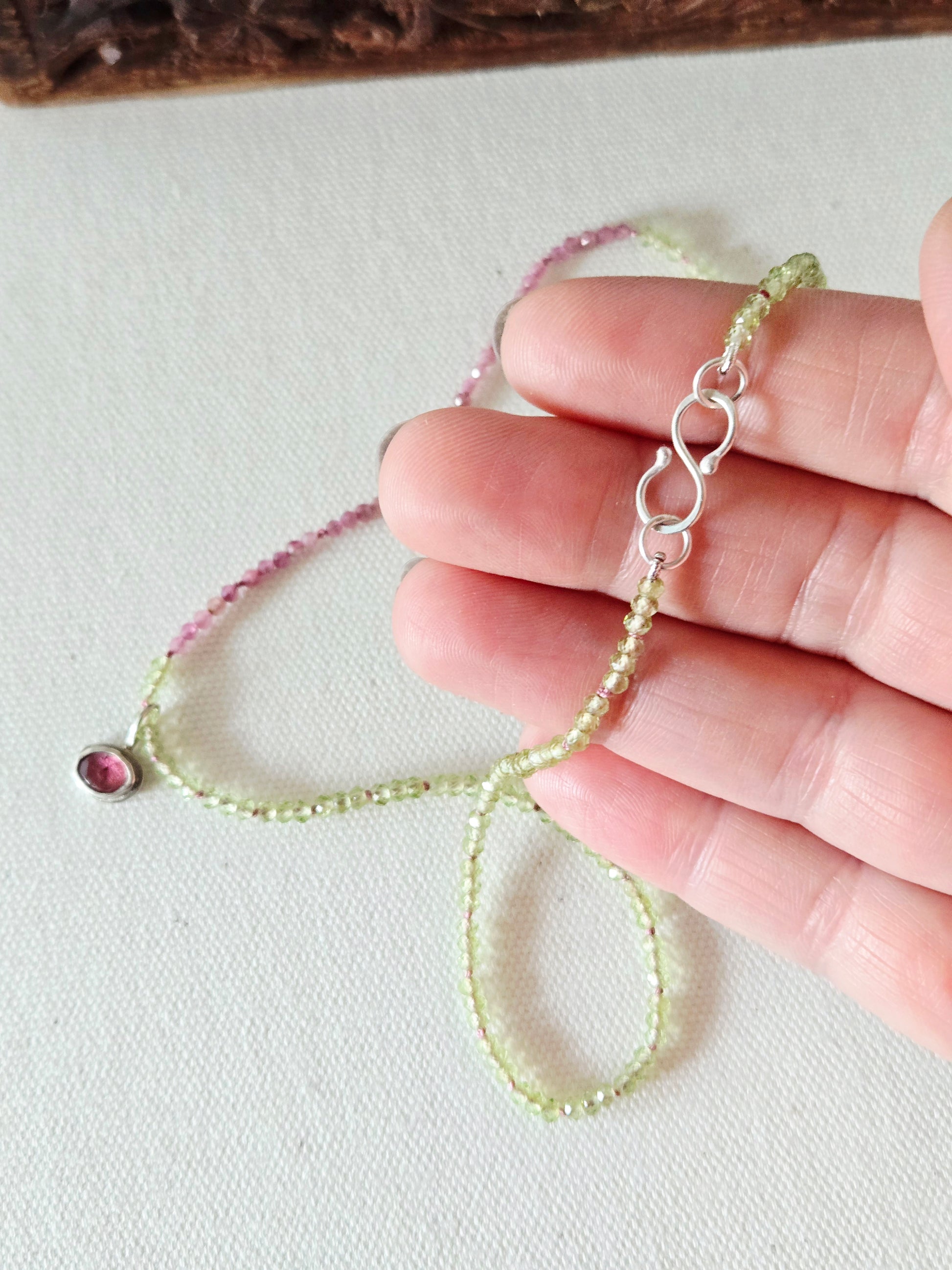 Hand holding a delicate necklace with a gemstone on a light background