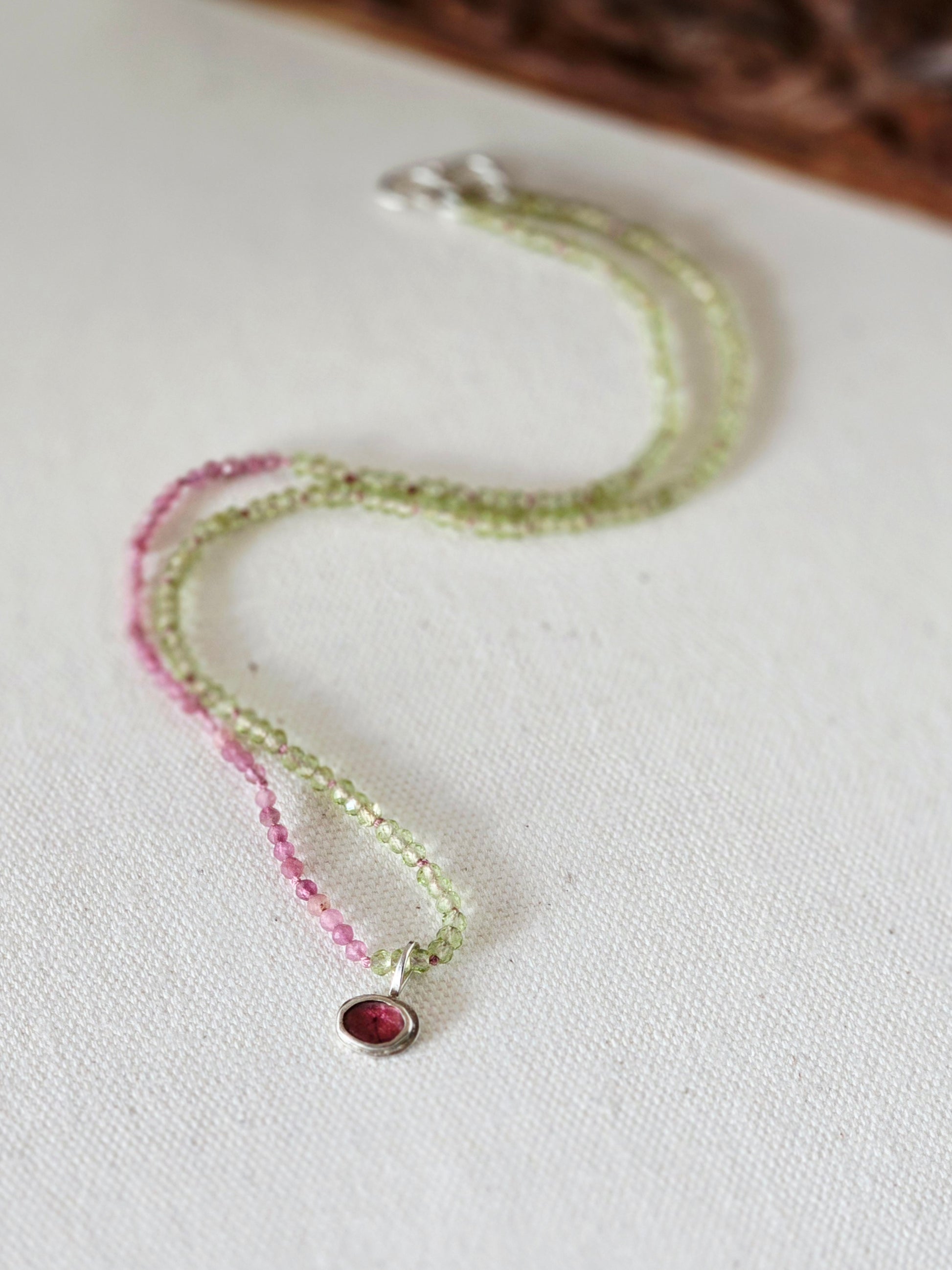 Necklace with pink and green beads on a white fabric background