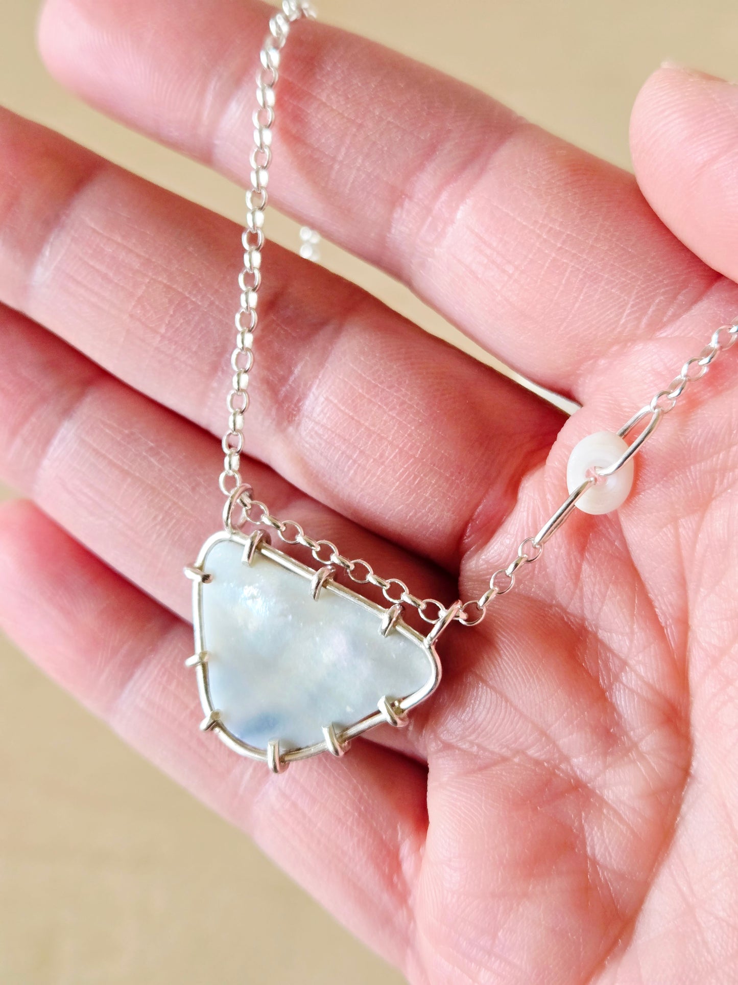Necklace with a shell pendant held in a hand against a beige background