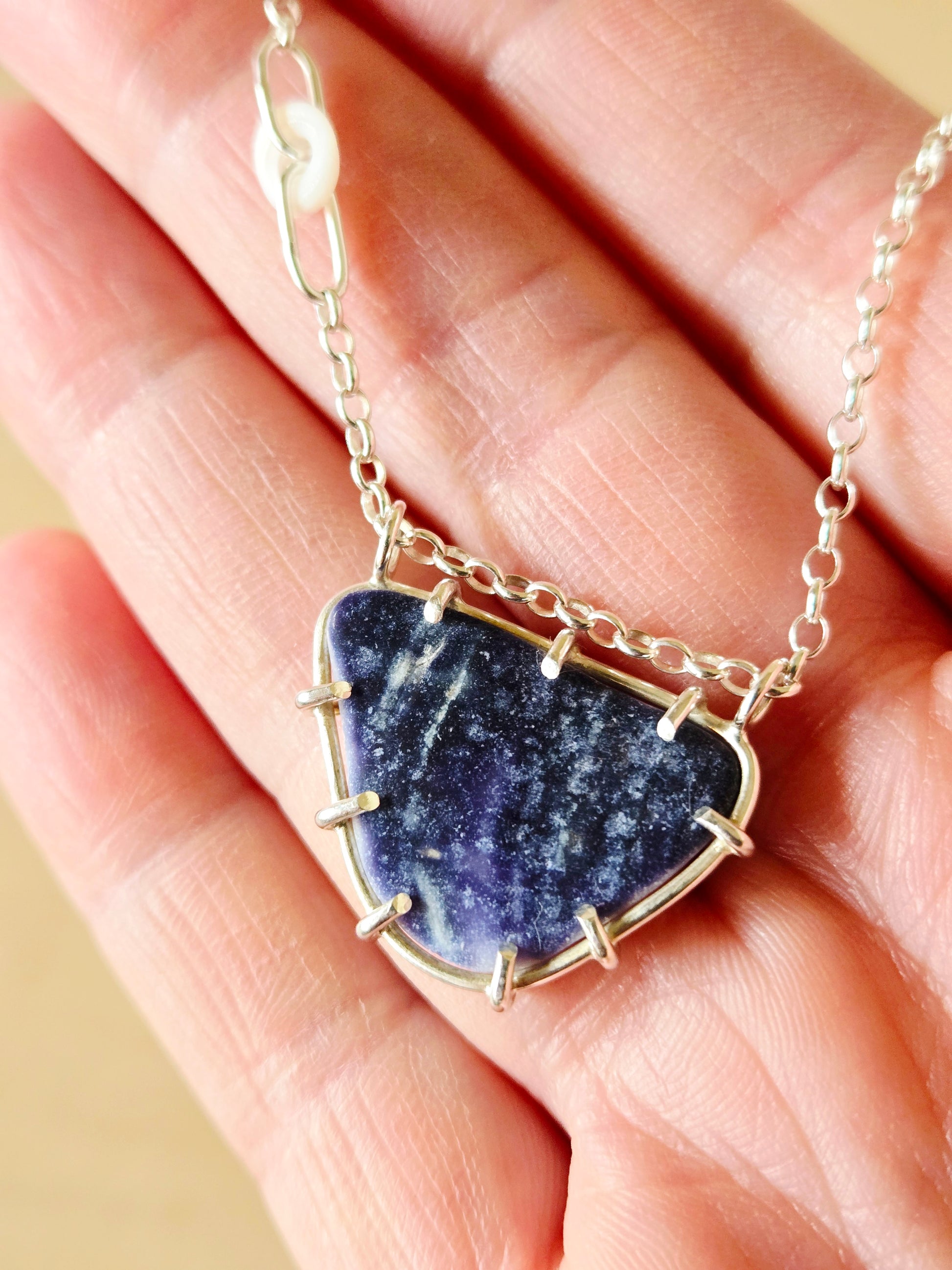 Necklace with a purple shell pendant held in a hand against a neutral background