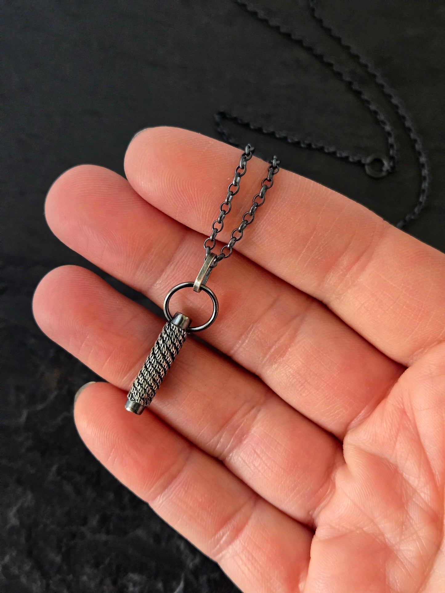 hand holding a black woven pendant necklace over a textured black background
