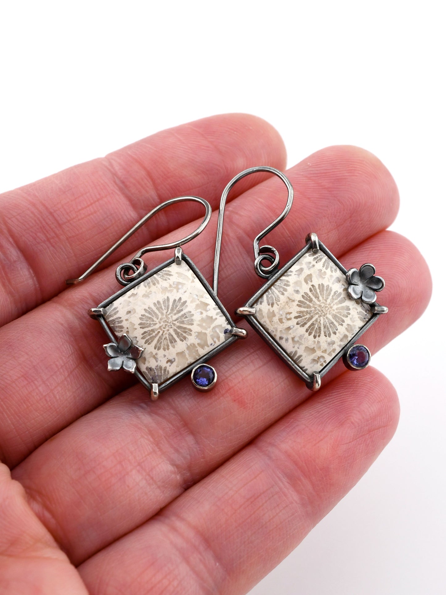 Silver earrings with floral designs held in a hand against a white background