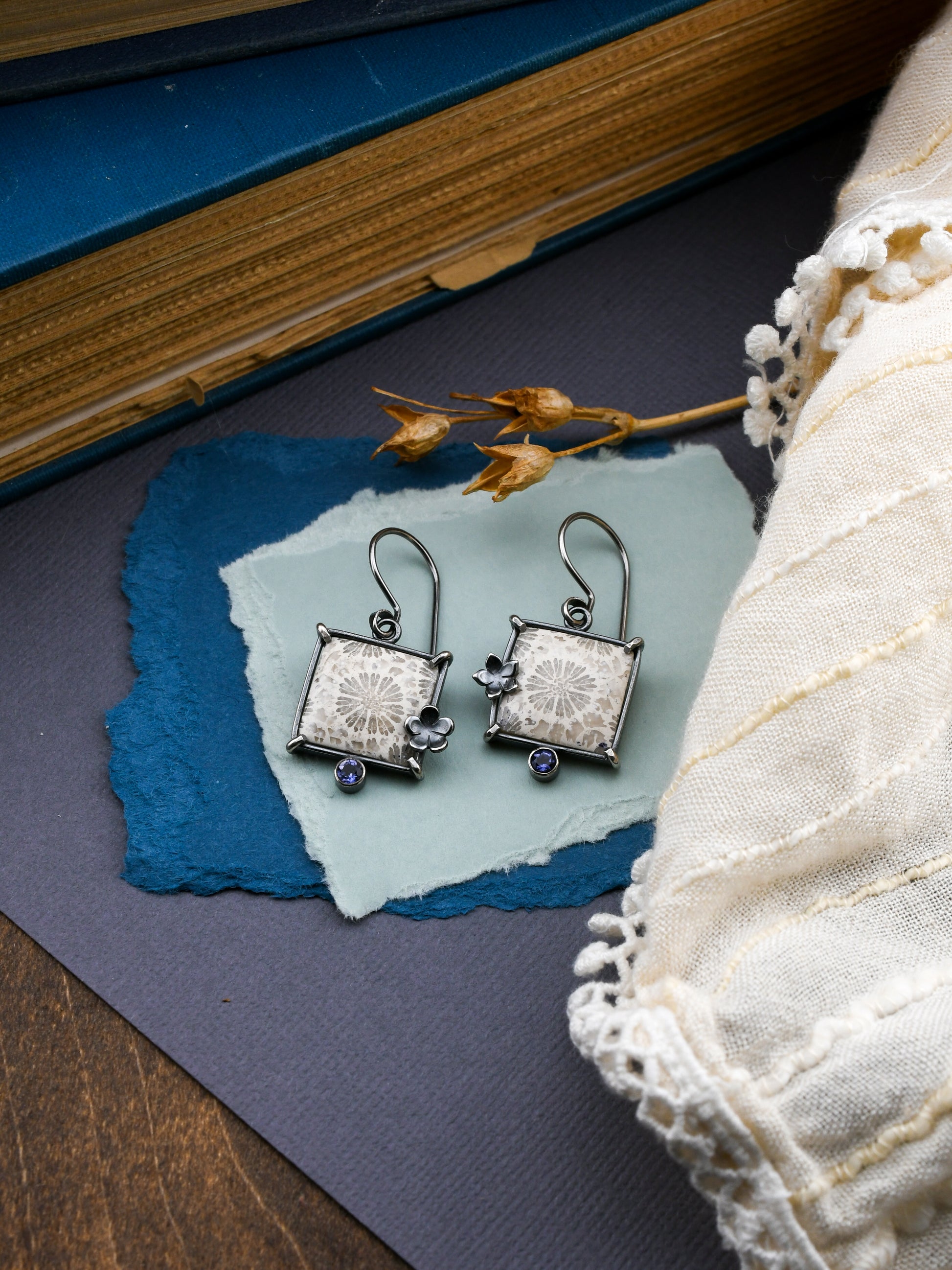 Pair of silver earrings on a blue paper with a book and lace fabric in the background