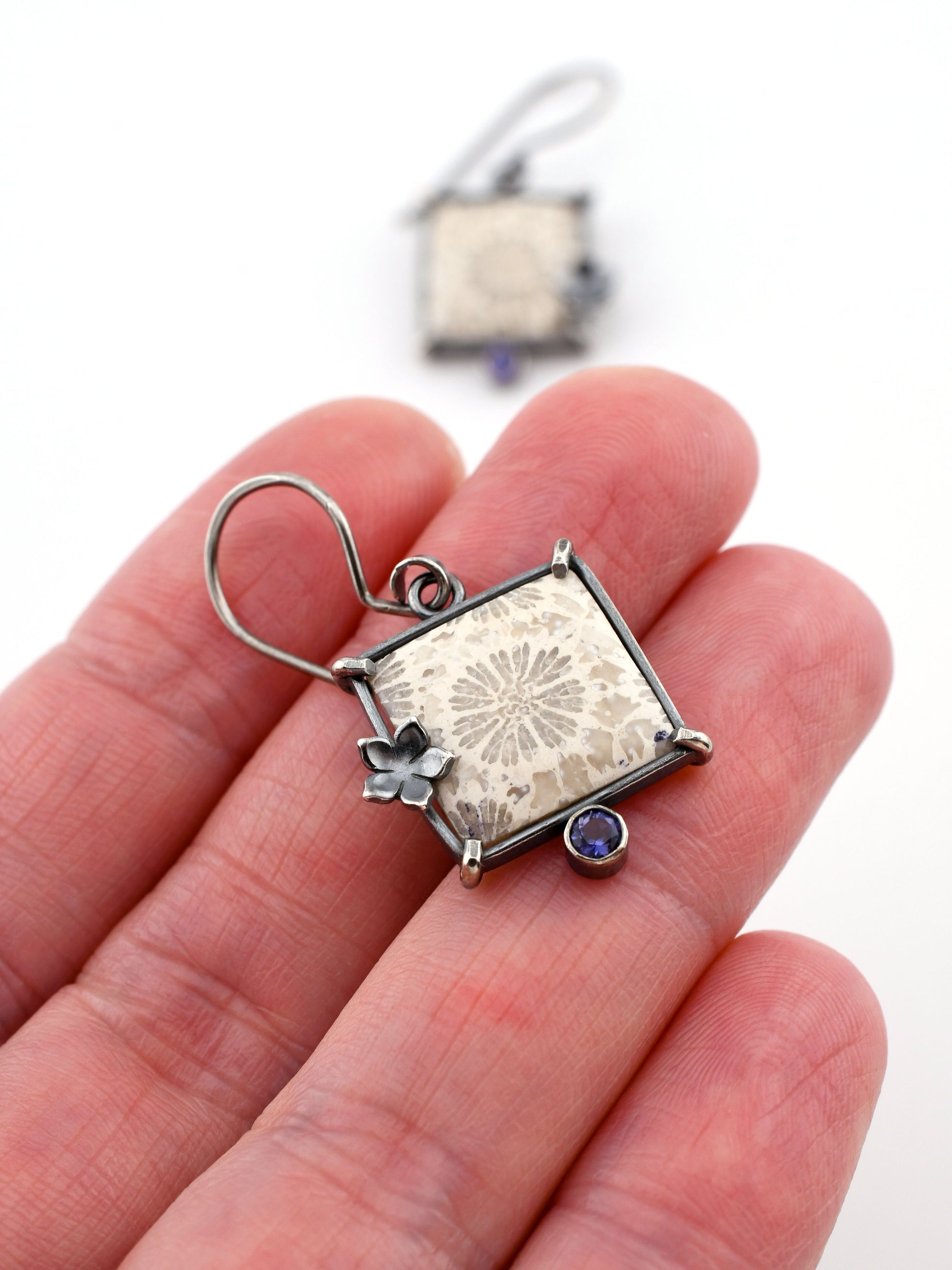Silver earring with floral design held in a hand against a white background