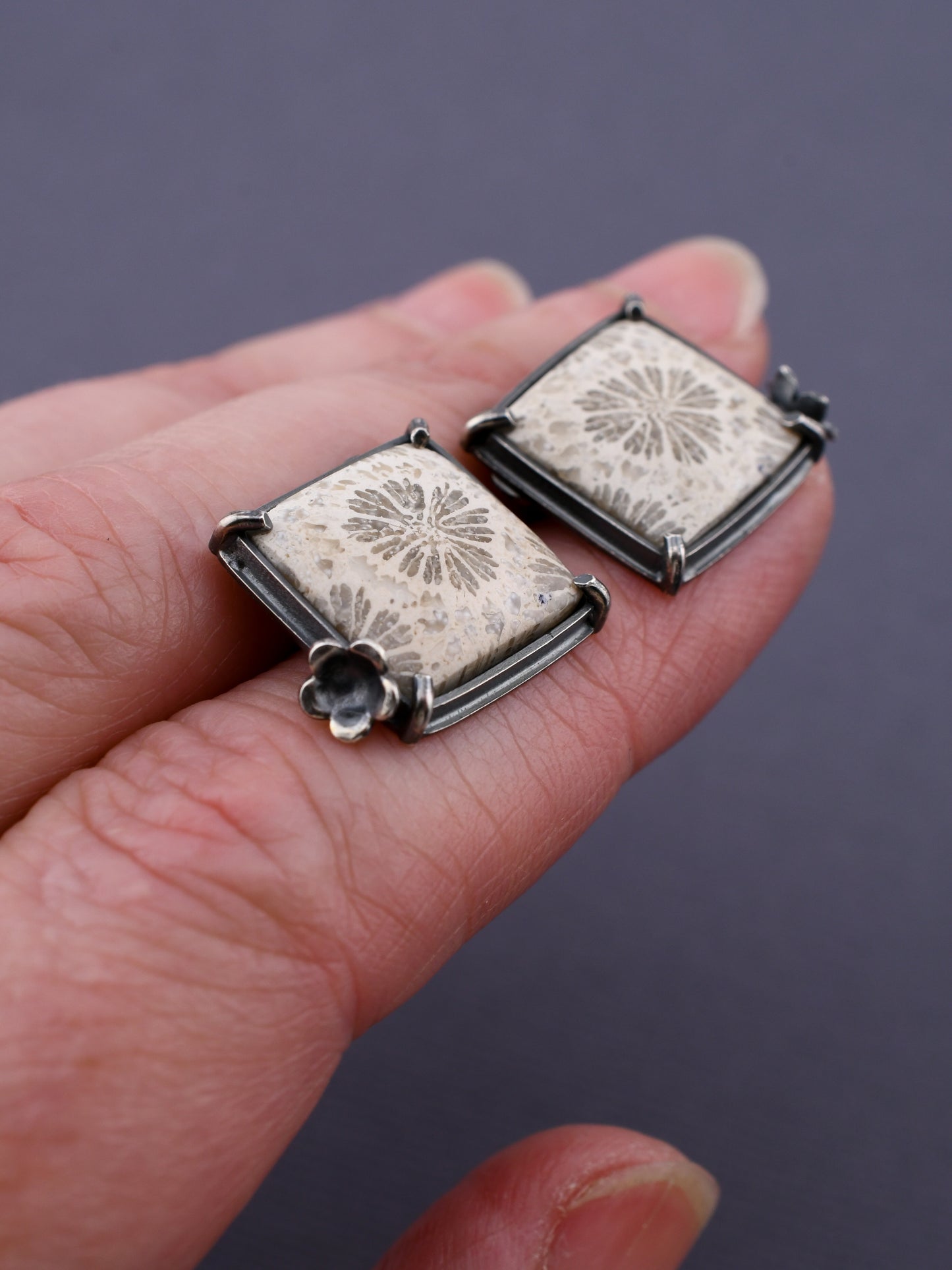 square stone earrings on a hand with a dark gray background