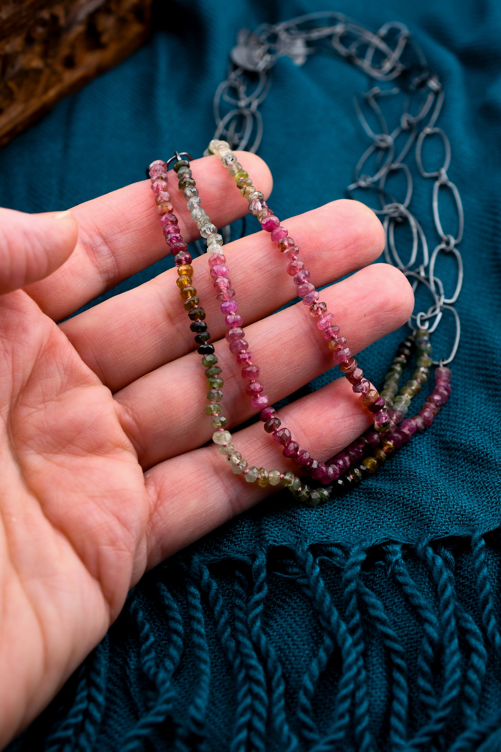 Hand holding three beaded necklaces with a teal fabric background